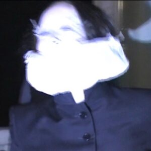 Allie X – Midnight for the Masses single cover: a blurred, flash-lit photo of a dark-haired figure whose face is blown out to white, wearing a navy buttoned jacket against a dark background
