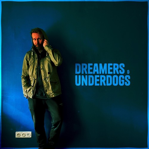 Ferus Melek – Dreamers & Underdogs album cover: a man in a hooded olive jacket leaning against a deep blue wall, with the title in bright blue capitals beside him