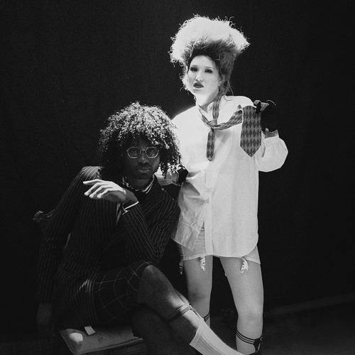 Haute & Freddy – Film Noir single cover: a black-and-white photo of the duo, one seated in a pinstripe suit and glasses, the other standing behind in a white shirt, loose tie and towering hair