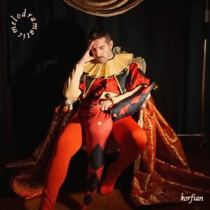 Korfian – Melodramatic single cover: Korfian dressed as a red and black harlequin court jester with a ruffled collar, slumped on a gilded throne draped in gold brocade