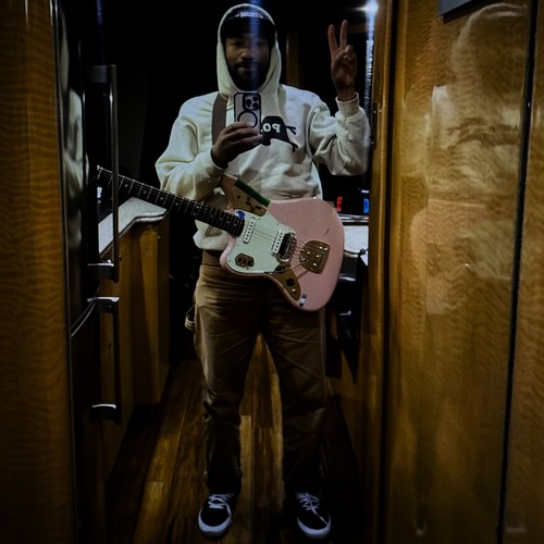 San Gabriel – Beside Me single cover: a dim mirror selfie of a musician in a white hoodie, holding a phone and a pink electric guitar in a narrow wood-panelled corridor
