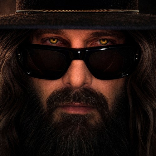 Sébastien Tellier – Loup (Remixes) cover: a close-up of Tellier in a dark brimmed hat, long hair and beard, with glowing yellow wolf eyes peering over black sunglasses